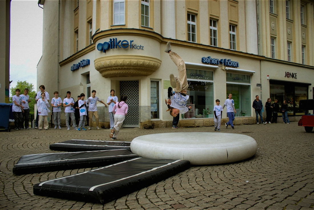 A person jumps over inflatable mats outdoors.