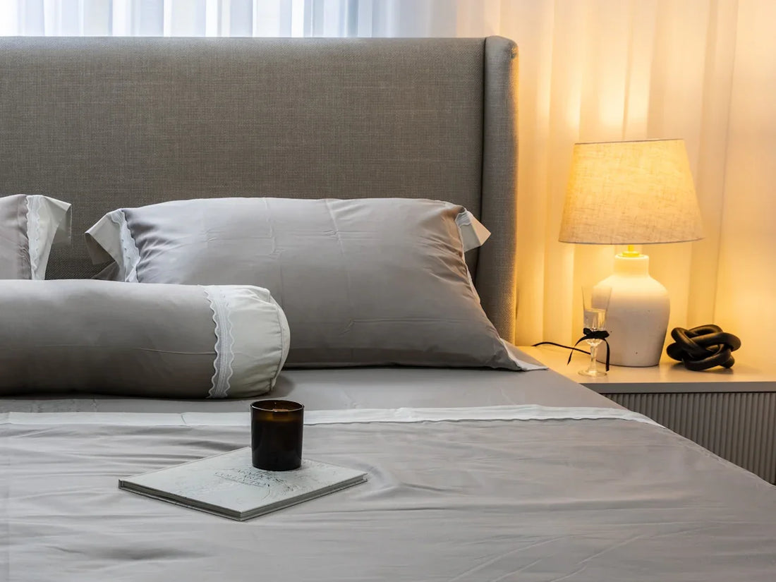 A neatly made bed with grey linens and pillows.