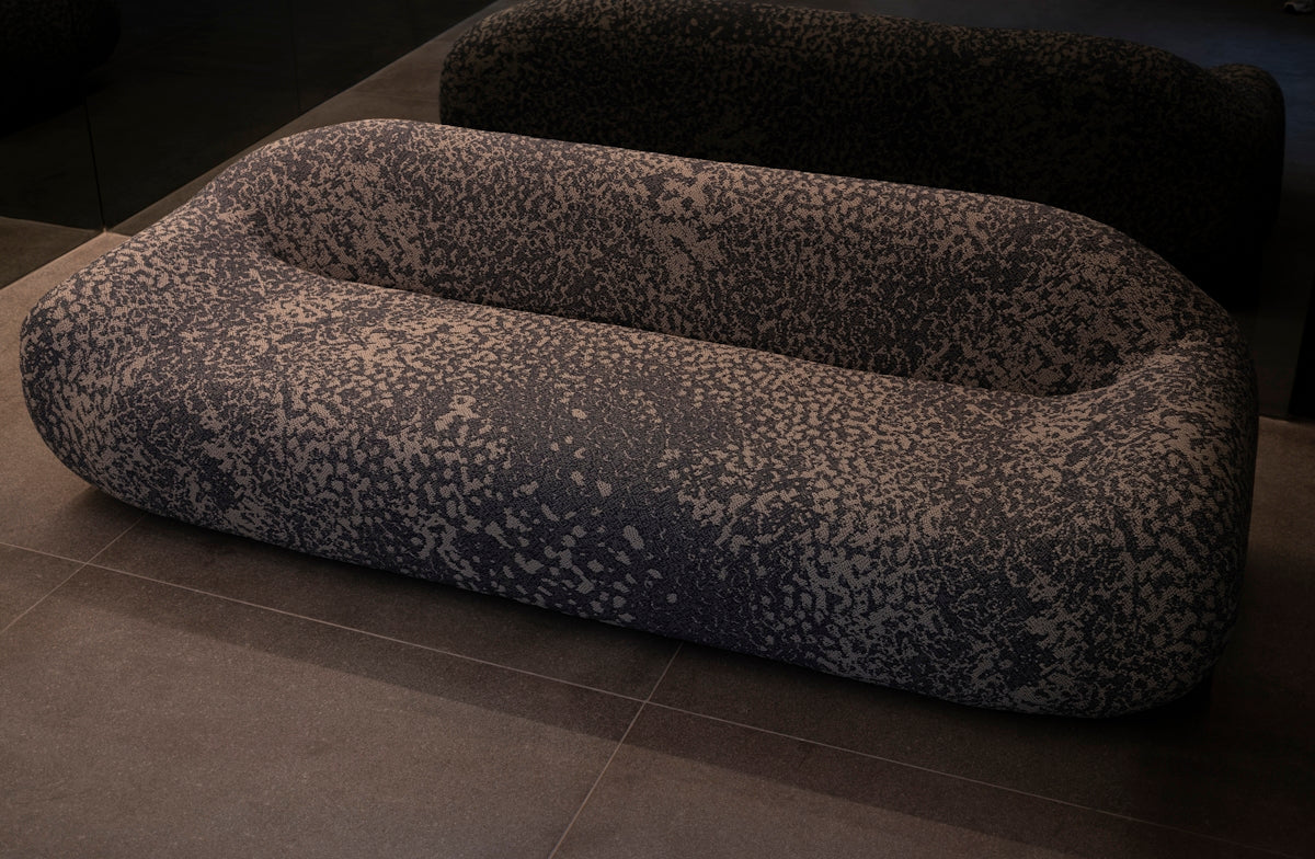 A uniquely shaped, patterned sofa on a tiled floor.