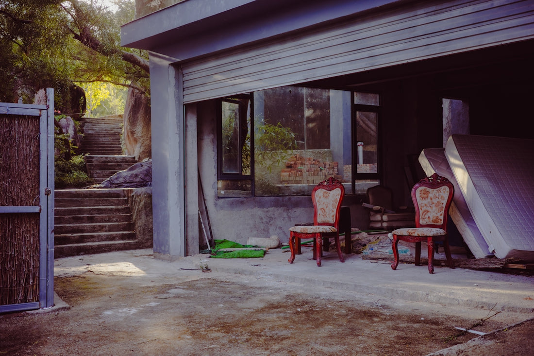 Two ornate chairs sit in a dusty garage entrance.