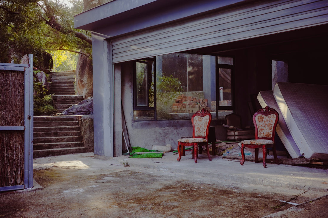 Two ornate chairs sit in a dusty garage entrance