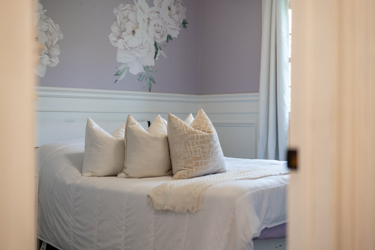 A bed with white pillows and floral wallpaper