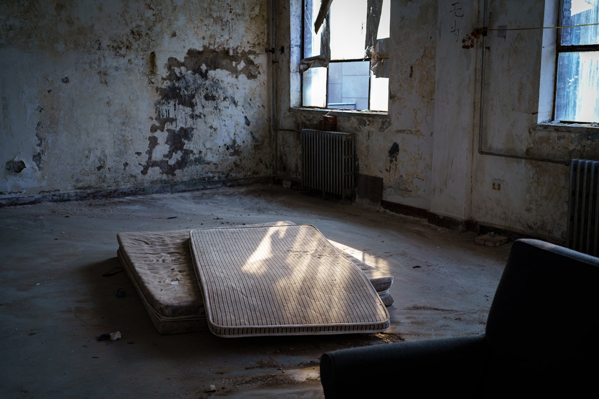Sunlit abandoned room with old mattresses and broken windows.