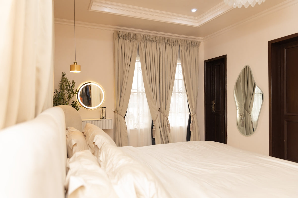 A bright bedroom with a large bed, windows, and mirrors.