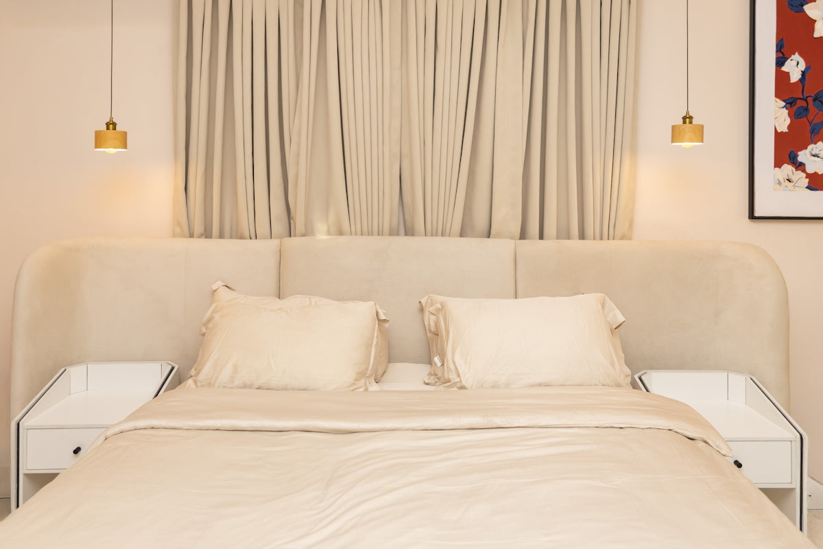 Elegant beige bed with white nightstands and pendant lights.