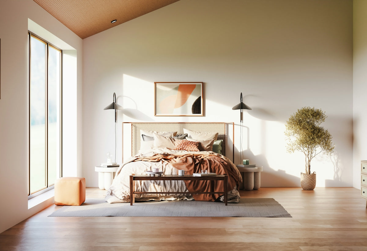 A sunlit bedroom with a bed, wooden bench, and potted tree on hardwood floors