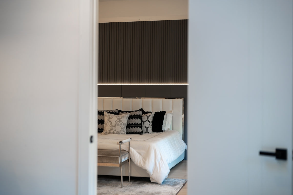 A view through a doorway into a bedroom with a white bed and dark wall