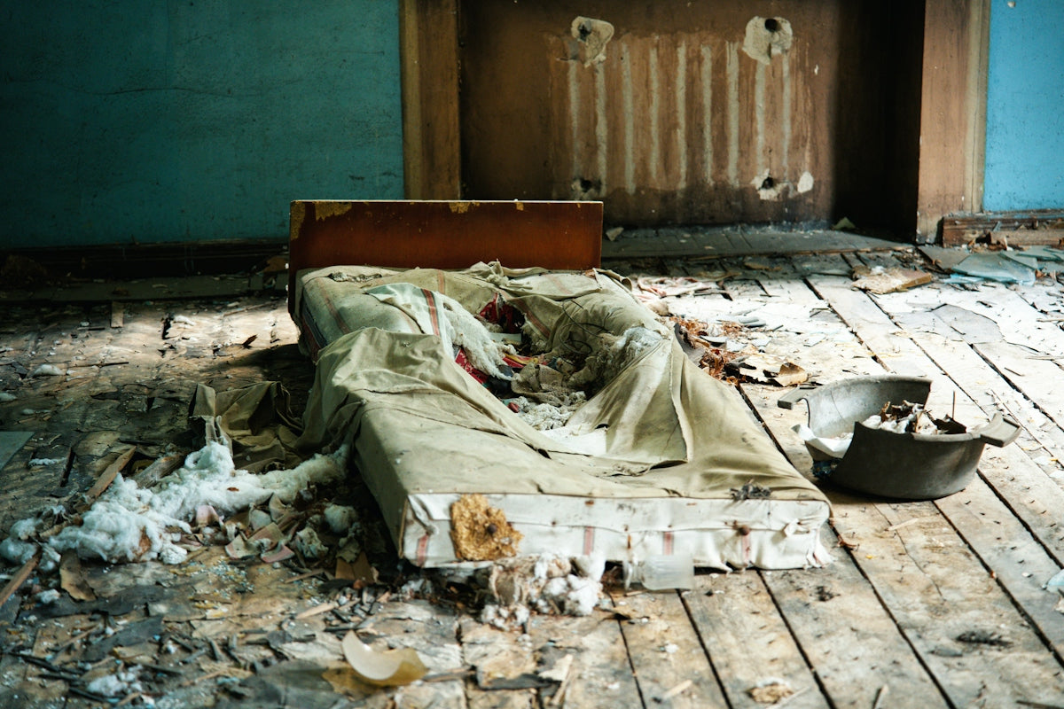 A damaged mattress on a wooden floor in a derelict room with blue walls