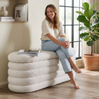 Boucle upholstered ottoman storage box with wooden legs, soft beige fabric, and padded top for seating and storage.