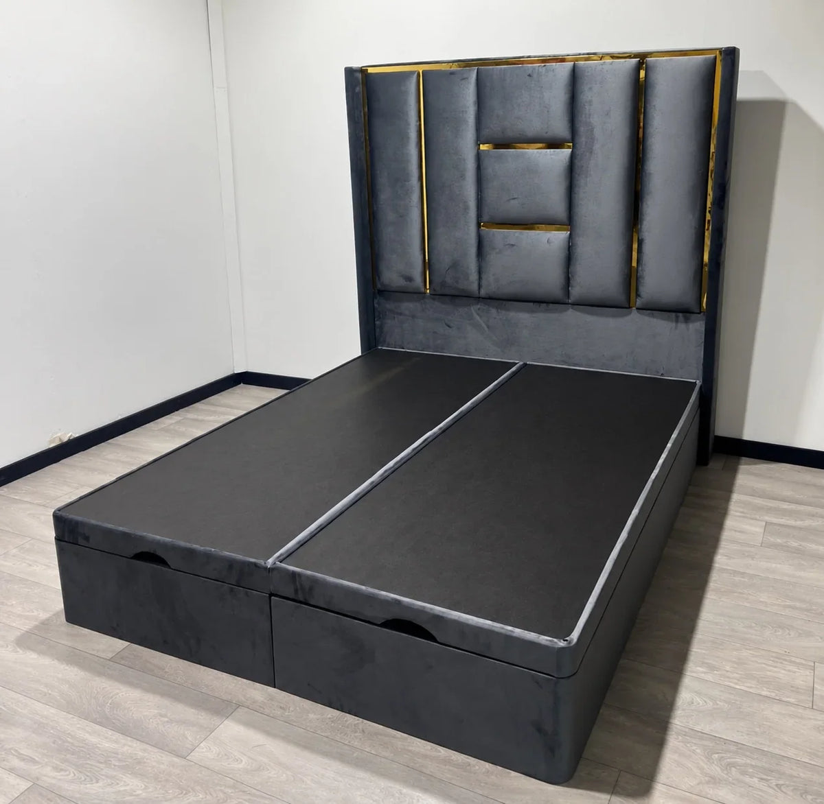 Angled view of the grey Luxe Panel Ottoman Bed with padded geometric headboard and gold trim